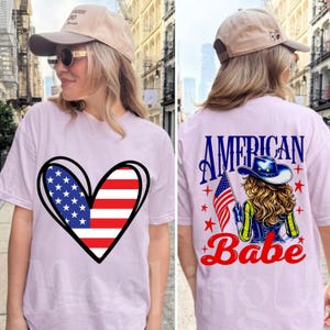 Peut inclure: T-shirt violet clair avec un motif de drapeau américain en forme de cœur sur le devant. Le dos du t-shirt affiche les mots "AMERICAN Babe" avec un dessin d'une femme tenant un drapeau américain, des étoiles et un chapeau de cow-boy.