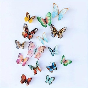 May include: A collection of colorful butterfly decorations in various sizes and patterns. The butterflies feature a range of colors, including orange, blue, green, and pink, with detailed wing designs. They are arranged on a white background.