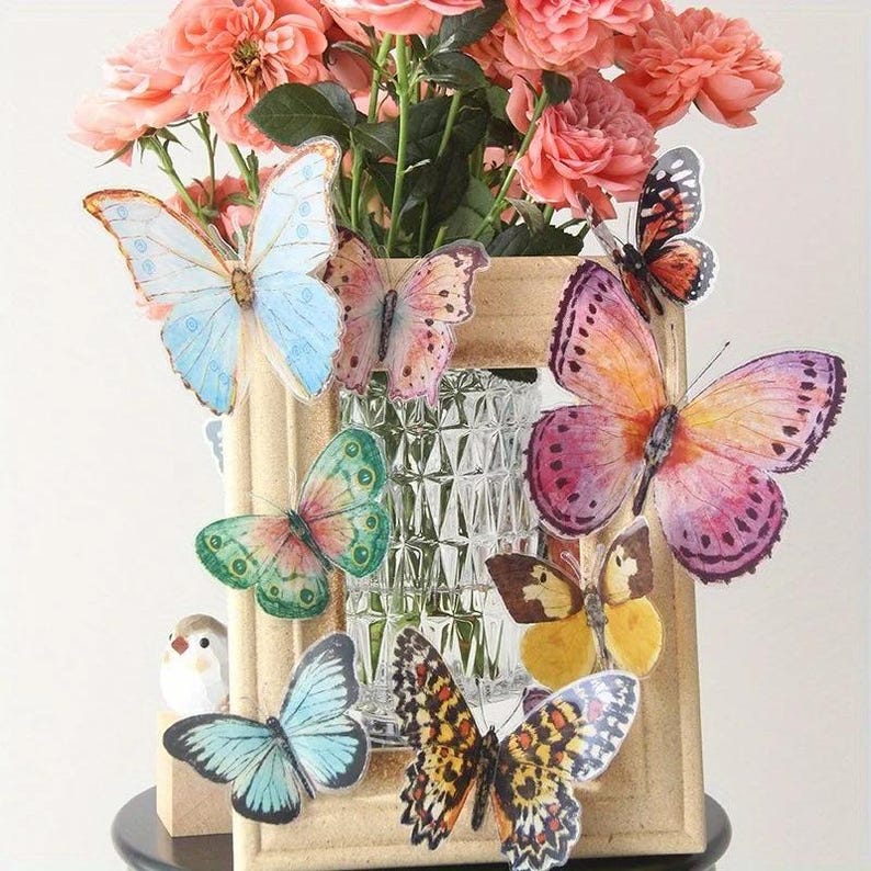 May include: A decorative arrangement featuring a wooden frame, a glass vase, and a bouquet of pink roses. Colorful butterfly stickers in various sizes and patterns are attached to the frame. The butterflies have shades of blue, green, pink, orange, and yellow.