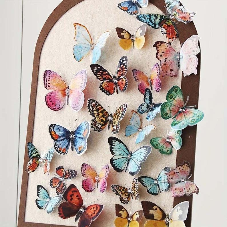 May include: A collection of colorful butterfly decorations in various sizes and patterns. The butterflies are affixed to a light beige background within a brown arched frame. The butterflies feature shades of pink, blue, orange, and green.