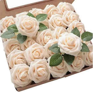 Könnte beinhalten: Eine Schachtel gefüllt mit elfenbeinfarbenen Kunstrosen. Jede Rose hat mehrere Blütenblätter und wird von grünen Blättern begleitet. Die Rosen sind eng angeordnet, wodurch ein voller und strukturierter Eindruck entsteht. Die Schachtel ist aus Pappe.