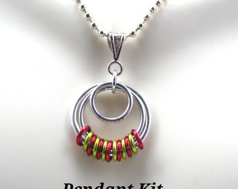 Puede incluir: Un collar con colgante plateado con tres anillos entrelazados. El anillo inferior está adornado con anillos rojos y verdes alternados. El collar tiene una cadena de bolas plateada y el texto "Pendant Kit" en la parte inferior.