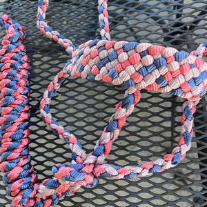 May include: Close-up of a braided rope halter in shades of pink, blue, and beige. The halter is made of tightly woven material, with a diamond-patterned background. The rope is designed for equine use.