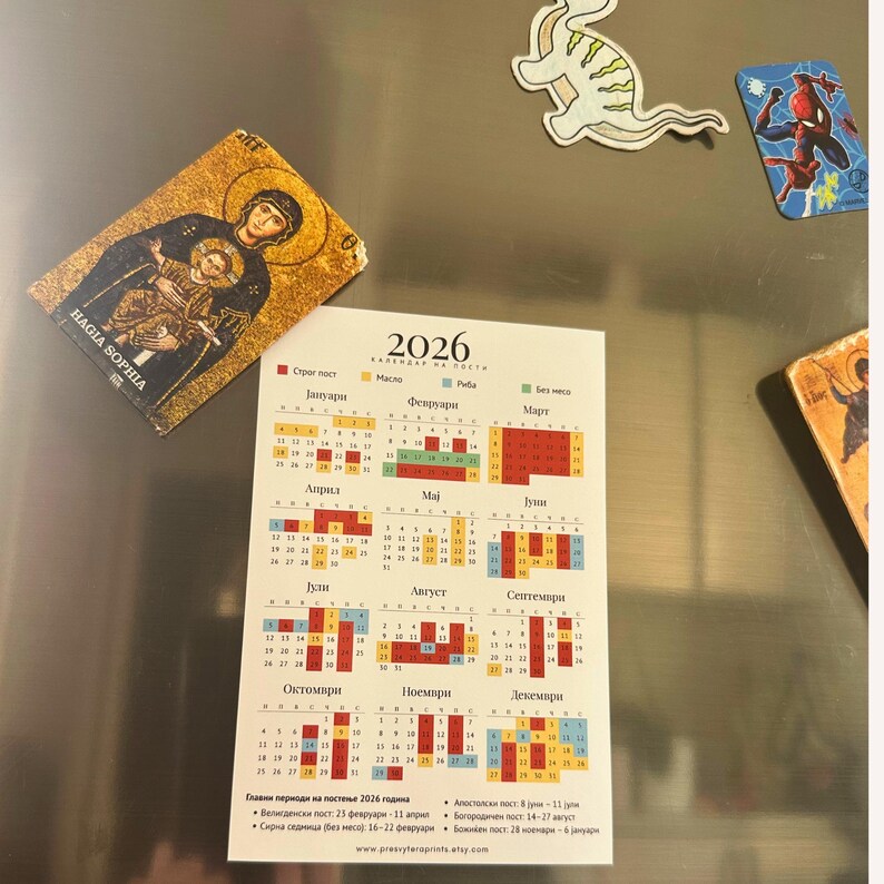 May include: A 2026 calendar with a religious theme, featuring a gold-toned icon of a religious figure and child, and several decorative magnets. The calendar is in a foreign language, with months and dates displayed.