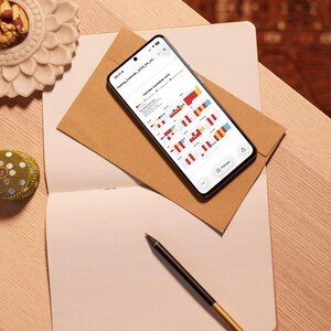 May include: A smartphone displaying a colorful calendar, resting on a brown envelope and a blank notebook. A black pen with a gold tip lies nearby. The calendar is labeled "Fasting Calendar 2023 EN A4". The scene is set on a light wooden surface.