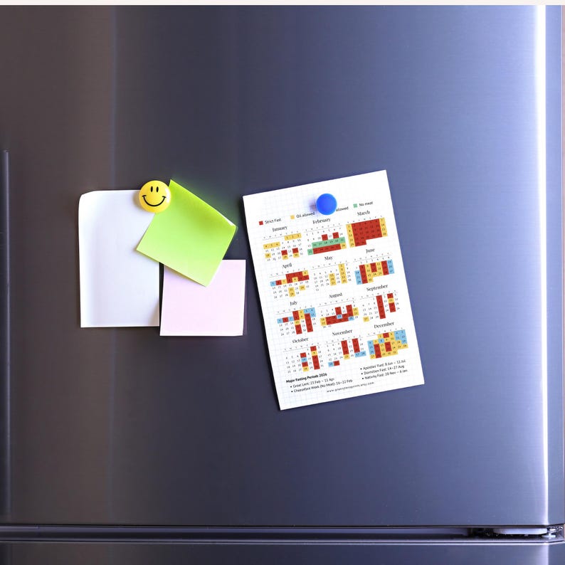 May include: A calendar printout with a colorful grid, held by a blue magnet on a silver refrigerator. The calendar displays monthly schedules with color-coded blocks. Beside the calendar are sticky notes and a smiley face magnet.