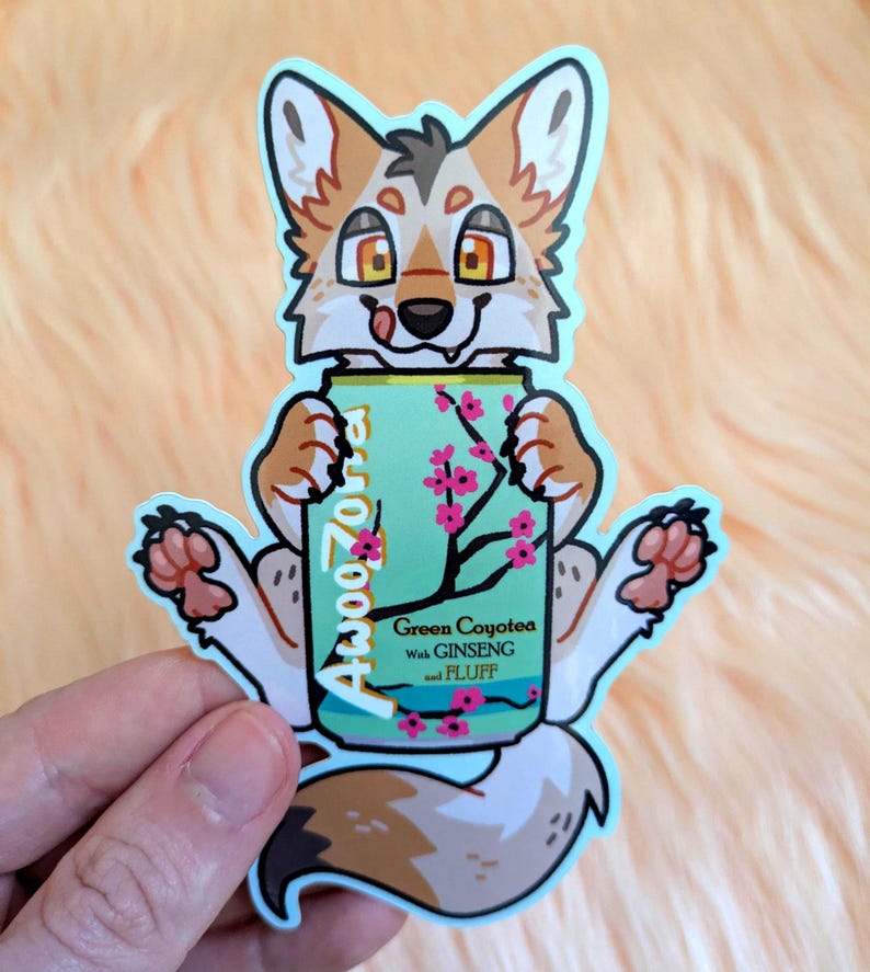 May include: A die-cut sticker featuring a cartoon fox with tan and white fur holding a light green beverage can. The can displays the text AwooZona, Green CoyoTea with GINSENG and FLUFF, and a graphic of a cherry blossom branch with pink flowers.