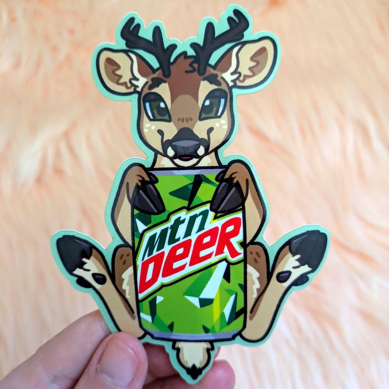 May include: A die-cut sticker featuring a cartoon deer with brown fur and dark antlers, holding a green soda can with the text mtn deer printed in white and red letters. The sticker has a light mint green border and a white outline.