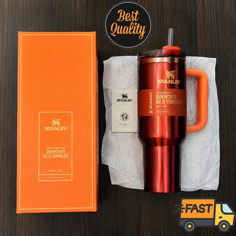 May include: A metallic red Stanley Quencher H2.0 tumbler with an orange handle and straw, accompanied by its orange retail box and a small product information card. The tumbler features a branded band with the text The Flowstate Quencher H2.0.
