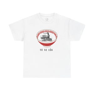 May include: A white short-sleeve t-shirt featuring a graphic of a red and white bowl containing a black and white steam locomotive. The bowl has a red geometric border pattern. Below the bowl, the text "TÔ XE LỬA" is printed in black.