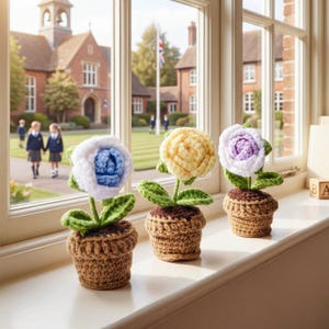 May include: Three crocheted flower arrangements in small brown pots sit on a windowsill. The flowers are white with blue, yellow, and purple centers, with green leaves and stems. The background shows a school building and children.