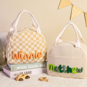 Pu&ograve; includere: Due borse per il pranzo con manici bianchi. Una &egrave; a scacchi gialli e bianchi con il nome "Winnie" in filo arancione. L'altra &egrave; in velluto a coste color crema con il nome "Matthew" in filo verde. Entrambe le borse hanno una tasca frontale.