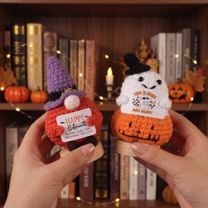 May include: Two crocheted figures on wooden bases. The left figure is a round orange gnome with a purple witch hat holding a sign that reads Happy Halloween Gnome body does Halloween like you. The right figure is a white ghost on an orange pumpkin base holding a sign that reads This is some boo sheet.