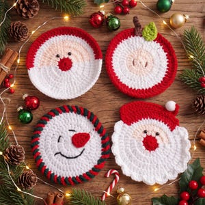 Puede incluir: Cuatro posavasos redondos de ganchillo con diseños navideños: una cara de Papá Noel con gorro rojo, una manzana roja con hoja verde, un muñeco de nieve con borde a rayas y un Papá Noel con gorro rojo y un pompón blanco.