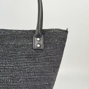 Può includere: Borsa tote nera intrecciata con manici in pelle nera. La borsa presenta un design strutturato a trama aperta. I manici sono attaccati con un piccolo pezzo di pelle fissato da due rivetti color argento. La borsa è progettata per trasportare oggetti.