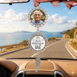 May include: A silver car charm with a photo of a man in a blue shirt, and a circular pendant with the text "I HAVE AN ANGEL WATCHING OVER ME I CALL HIM DAD". A silver wing charm hangs below.