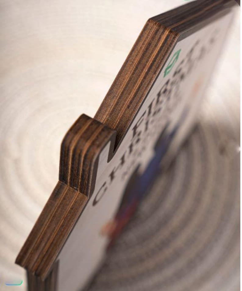 May include: Wooden sign with the text "FIRST CHRISTMAS" in a decorative font. The sign has a dark brown, layered wood edge and a white face with colorful accents. The sign is angled, showing the side and front.