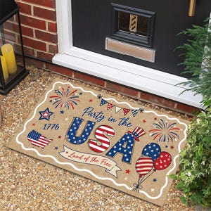May include: A rectangular doormat with a patriotic theme. The mat features the text "Party in the USA" and "Land of the Free" with red, white, and blue stars and stripes. It includes images of fireworks, balloons, and the American flag.