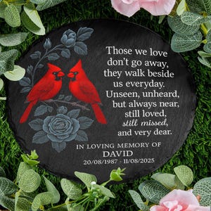 May include: A round, black memorial stone with a pair of red cardinals perched on a branch, surrounded by floral accents. The inscription reads "Those we love don't go away..." and includes a name and dates.