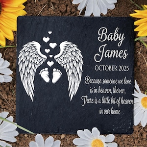 May include: A black slate memorial stone with white text and graphics. The design includes angel wings, hearts, and baby footprints. The text reads "Baby James OCTOBER 2025" and a sentimental quote.