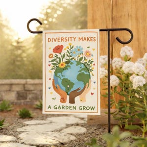 May include: A garden flag with the text "DIVERSITY MAKES A GARDEN GROW." The flag features a globe held by hands of different skin tones, surrounded by colorful flowers. The flag is displayed on a black metal garden stake.
