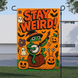 Puede incluir: Bandera de jardín de Halloween naranja con las palabras "STAY WEIRD!" y una rana de dibujos animados tocando el banjo mientras monta un caracol. La bandera también presenta fantasmas, murciélagos, calabazas y estrellas.
