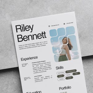 May include: A white resume with the name "Riley Bennett" in large black font. The resume includes sections for experience, skills, and portfolio. A photo of a person is in the upper right corner, and the resume is on a gray surface.