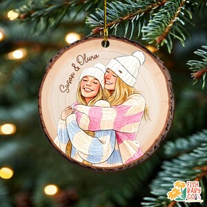 May include: A wooden Christmas ornament with a bark edge. The ornament features an illustration of two smiling people wearing white beanies and striped sweaters, embracing. The names "Susan & Olivia" are written on the ornament.