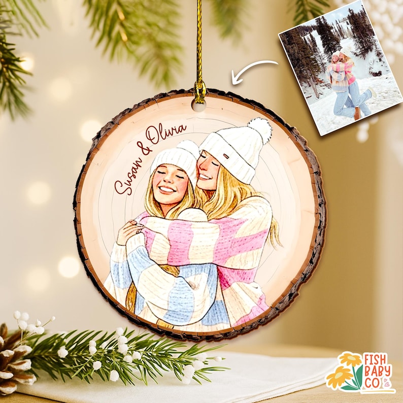 May include: A wooden Christmas ornament with a drawing of two women hugging, wearing winter hats and sweaters. The ornament has the names "Susan & Olivia" written on it. A small photo of the women hugging in the snow is also included.