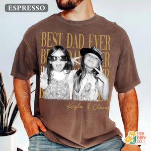 Puede incluir: Camiseta color caf&eacute; con la frase dorada "BEST DAD EVER". La camiseta presenta una foto en blanco y negro de dos ni&ntilde;as. Los nombres "Kayla & Clara" est&aacute;n impresos debajo. La camiseta es de corte holgado.
