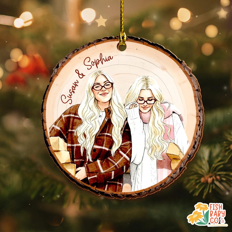 May include: A round wooden Christmas ornament with a watercolor illustration of two women, one in a plaid jacket and the other in a white sweater. The ornament has the names "Susan & Sophia" written on it. The ornament is hanging from a gold string.