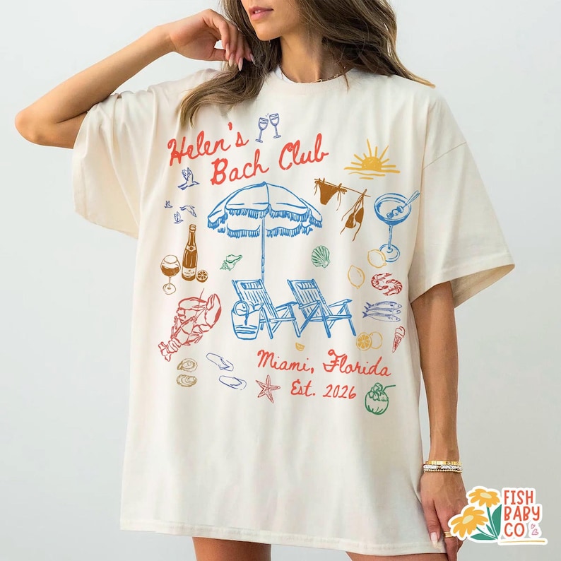 May include: An off-white short-sleeve t-shirt featuring a colorful graphic print with the text "Helen's Bach Club" and "Miami, Florida Est. 2026". The design includes illustrations of a beach umbrella, lounge chairs, a lobster, drinks, and seashells.