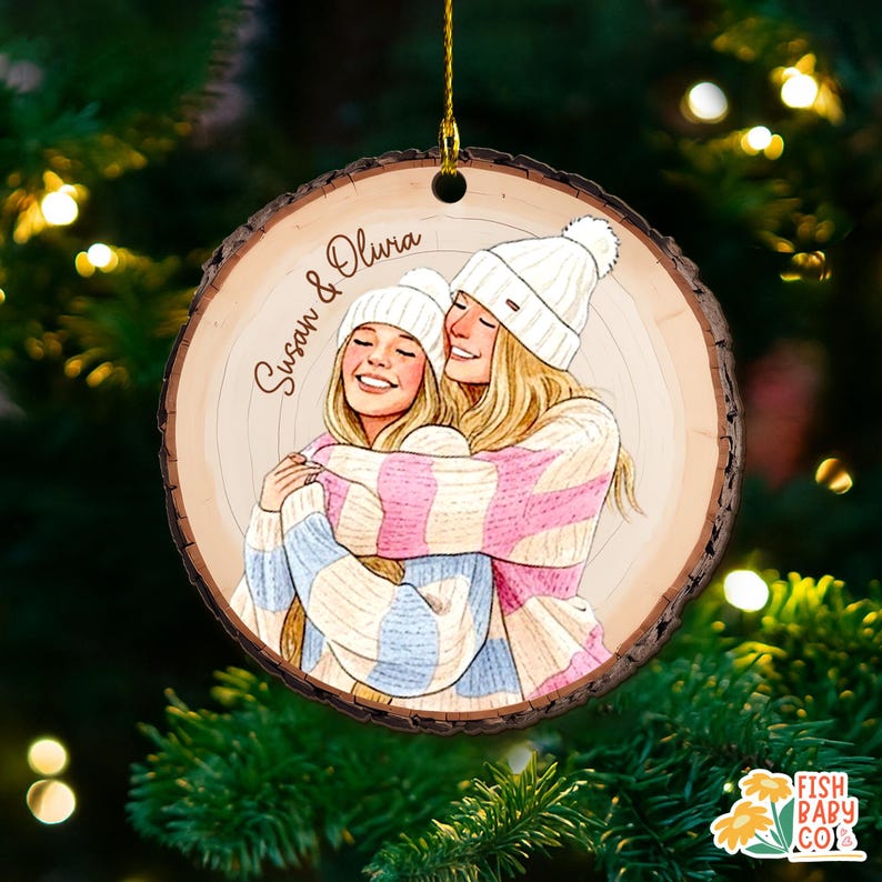 May include: A wooden Christmas ornament with a drawing of two women hugging, wearing white beanies and striped sweaters in pink, blue, and cream. The ornament has the names "Susan & Olivia" written on it.