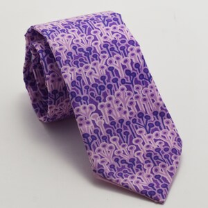 May include: A purple tie with a repeating pattern of small, stylized flowers. The tie is made of a smooth fabric and has a pointed tip.