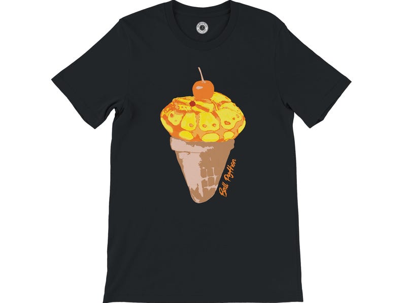 K&ouml;nnte beinhalten: Schwarzes T-Shirt mit einer Grafik einer Eist&uuml;te. Das Eis hat ein gelb-oranges Muster, gekr&ouml;nt von einer Kirsche. Die Waffel ist braun, und der Text "Ball Python" ist orange geschrieben.