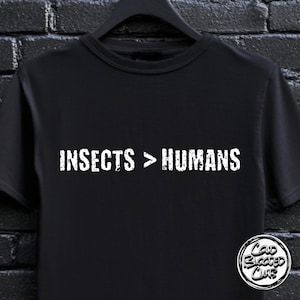 May include: Black t-shirt with the white text "INSECTS > HUMANS" across the chest. The shirt has a crew neck and short sleeves. A circular logo with the text "Cold Blooded Club" is on the bottom right.