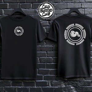 May include: Black t-shirts with a circular graphic featuring a snake and the text "Hognose" repeated around the edge. The front of the shirt has a smaller version of the graphic. The shirts are hanging against a dark brick wall.