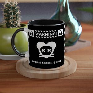 May include: Black ceramic mug with a white graphic of a mouse with an "X" for eyes, and the text "Rodent thawing mug". The mug has a black interior and handle, and the word "WARNING!" is printed at the top.