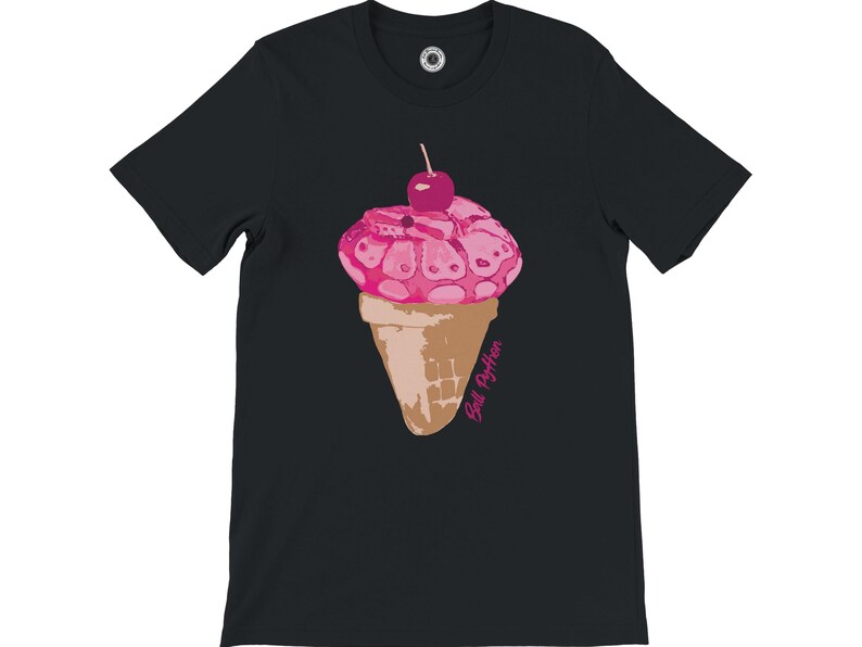 K&ouml;nnte beinhalten: Schwarzes T-Shirt mit einem Design einer rosa Eist&uuml;te und einer Kirsche. Das Eis hat ein einzigartiges Muster, und die Waffel ist hellbraun. Der Text "Ball Python" ist in Rosa auf der Waffel aufgedruckt.