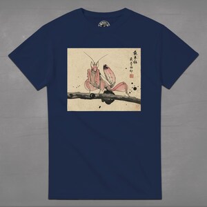 May include: Navy blue t-shirt featuring a Japanese-style illustration of a pink orchid mantis perched on a branch. The artwork includes Japanese characters and ink splatter details, creating a unique design.
