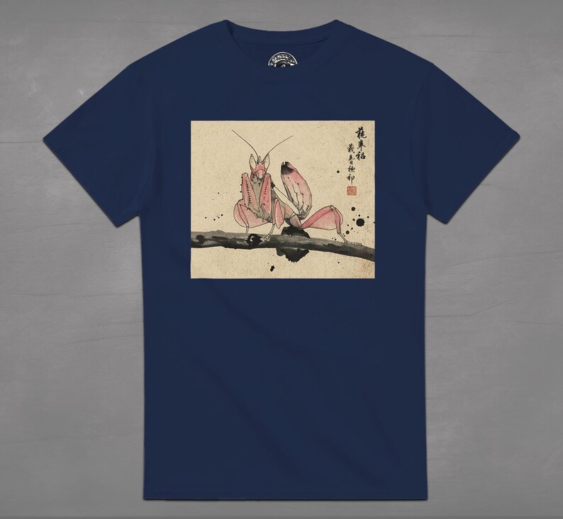 May include: Navy blue t-shirt featuring a Japanese-style illustration of a pink orchid mantis perched on a branch. The artwork includes Japanese characters and ink splatter details, creating a unique design.