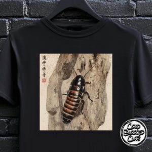 Könnte beinhalten: Schwarzes T-Shirt mit einer detaillierten Illustration einer Kakerlake auf einem Baumstamm. Das Insekt hat einen schwarzen Kopf und einen segmentierten, rotbraunen Hinterleib. Das Shirt hat auch japanischen Text und ein Cold Blooded Club-Logo.