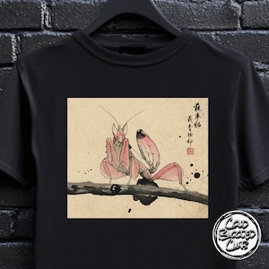 May include: Black t-shirt featuring a pink praying mantis illustration in a Japanese art style. The insect is perched on a branch, with Japanese characters in the upper right corner. The shirt also has a "Cold Blooded Club" logo.