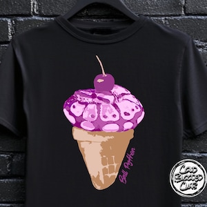 Peut inclure: T-shirt noir avec un motif de cornet de glace violet surmonté d'une cerise. La glace présente un motif de serpent et le cornet est marron. Le texte "Ball Python" est écrit en rose sur le côté.