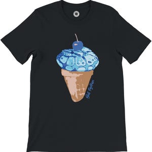 K&ouml;nnte beinhalten: Schwarzes T-Shirt mit einem Design einer blauen Eist&uuml;te und einer Kirsche. Das Eis hat ein schlangenartiges Muster. Die Waffel ist braun. Der Text "Still Python" steht in Blau auf der Waffel.