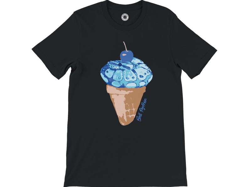 K&ouml;nnte beinhalten: Schwarzes T-Shirt mit einem Design einer blauen Eist&uuml;te und einer Kirsche. Das Eis hat ein schlangenartiges Muster. Die Waffel ist braun. Der Text "Still Python" steht in Blau auf der Waffel.