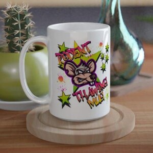 Könnte beinhalten: Weiße Keramik-Tasse mit einem Cartoon-Ratten-Design und dem Schriftzug "RODENT THAWING MUG" in Graffiti-Schrift. Das Design umfasst grüne Sterne und orangefarbene Farbspritzer. Die Tasse hat einen weißen Henkel.