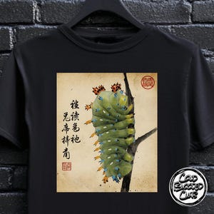 May include: Black t-shirt with a vintage-style illustration of a green caterpillar on a branch, accompanied by Japanese calligraphy and a red seal. The design has an artistic aesthetic.