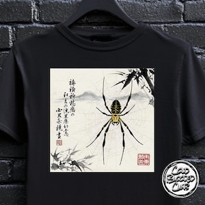May include: Black t-shirt with a Japanese-style illustration of a spider on a web, with Japanese text and a red seal. The spider is black and yellow. The shirt also has a "Cold Blooded Club" logo.