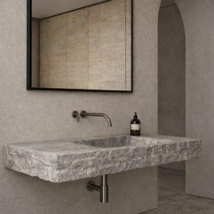May include: A modern bathroom sink made of gray stone. The sink has a rectangular shape with a built-in basin and a brushed metal faucet. A dark-framed mirror hangs above the sink, and a brown bottle sits on the countertop.